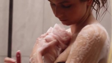 Duşta vücudunu sabunla yıkayan genç bir kadın. Esmer kız duş alırken sünger kullanıyor. Yüksek kaliteli FullHD görüntüler