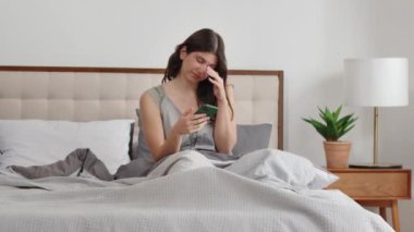 Yatakta oturan esmer bir kadın gözlerini ovuşturuyor ve telefonundaki haberlere bakıyor. Yeni uyanmış bir kadın elinde telefonuyla yatakta oturuyor ve verdiği uyarılara bakıyor.