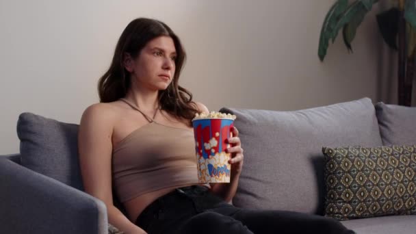 Piękna Młoda Brunetka Siedzi Kanapie Trzymając Ręku Szklankę Popcornu Ogląda — Wideo stockowe