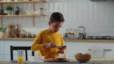 Küçük bir çocuk mutfakta kendine yabanmersinli reçelli sandviç yapıyor. Çocuk kendine bir sandviç yapar ve onu bir beslenme çantasına koyar. Yüksek kalite 4k görüntü