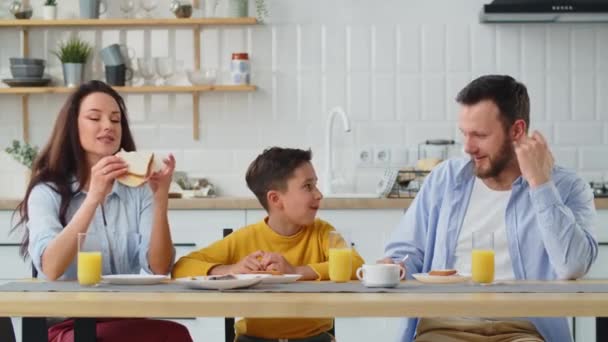 一个友善的家庭边坐着边开玩笑边谈论着什么 男孩一边吃三明治 一边与父母交流 坐在厨房的餐桌旁 高质量4K — 图库视频影像