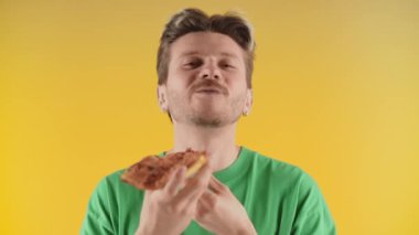 Pizzayı gözü kapalı çiğneyen mutlu genç adam. Heyecanlı adam sarı arka planda pizza dilimini seviyor. Yüksek kalite 4k görüntü