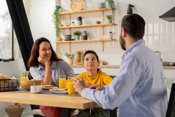 朝食中に男は息子と妻と通信する 家族はオレンジジュースのサンドイッチとガラスのプレートとキッチンテーブルに座っています 高品質の写真 — ストック写真