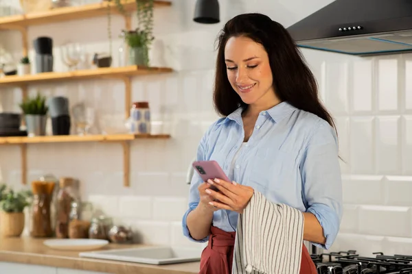 Uma Morena Sorridente Está Cozinha Olhando Para Algo Seu Smartphone — Fotografia de Stock