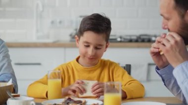 Adam ve ailesi kahvaltıda sandviç yiyorlar. Genç bir adam ailesiyle bir masaya oturur ve bir sandviç yer. Yüksek kalite 4k görüntü