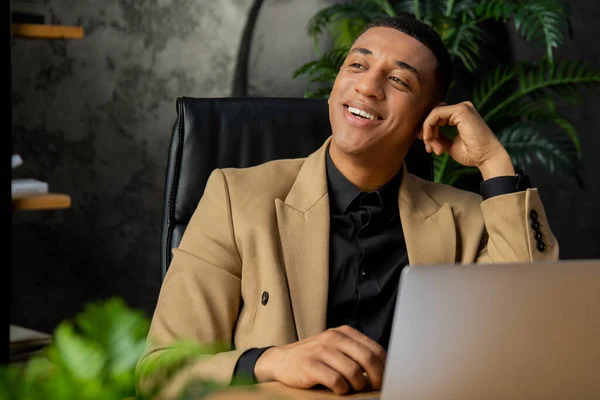 植物と居心地の良いオフィスでラップトップを使用してジャケットで黒のビジネスマンの笑顔 成功したアフリカ系アメリカ人起業家は仕事の日を楽しむ 高品質の写真 — ストック写真
