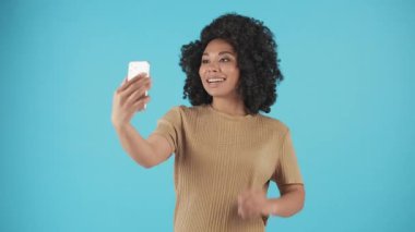 Çekici genç bir kadın mavi bir arka planda duruyor ve telefon kamerasıyla biriyle iletişim kuruyor. Bir kadın blogcu sosyal medya takipçileri için video mesajları kaydediyor. Yüksek kalite 4k görüntü