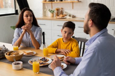 Küçük bir çocuk ailesiyle birlikte masada oturur ve bir şey söyleyen babasını dikkatle dinler. Çocuk anne ve babasıyla mutfak masasında kahvaltı ediyor. Yüksek kalite fotoğraf