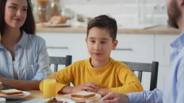 Genç bir adam ailesiyle bir masaya oturur ve portakal suyu içer. Sarı kazaklı bir çocuk mutfak masasında ailesiyle kahvaltı yapar. Yüksek kalite 4k görüntü