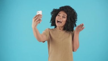 Çekici esmer tenli bir kız bir akıllı telefonun ön kamerasında kendi fotoğrafını çekiyor. Kız mavi bir duvarın arkasında duruyor ve selfie çekiyor. Yüksek kalite 4k görüntü