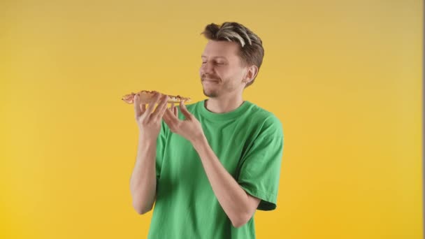 一个年轻人站在摄像机前 手里拿着一块披萨 一个穿着绿色T恤的年轻人喜欢吃他最爱吃的披萨 高质量的4K镜头 — 图库视频影像