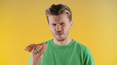 Kaşlarını çatan genç adam pizzadan bir ısırık alır ve olumsuz bir şekilde başını sallar. Yeşil tişörtlü bir adam pizzasından memnun değil. Yüksek kalite 4k görüntü