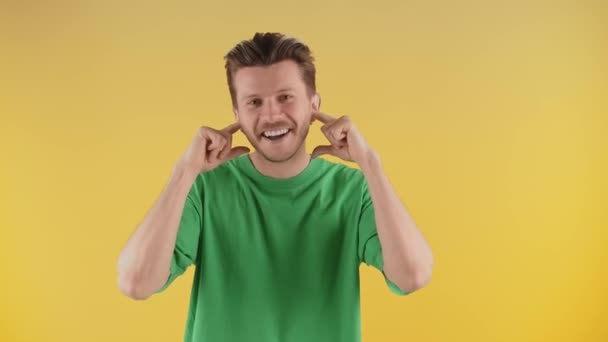 Улыбающийся Мужчина Позирует Перед Камерой Затыкая Уши Пальцами Парень Зелёной — стоковое видео