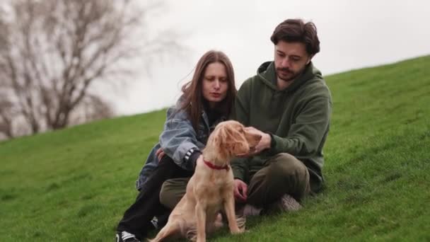 Jovem Casal Com Seu Cão Senta Grama Parque Homem Barbudo — Vídeo de Stock