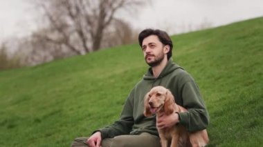 Sakallı bir esmer dışarıda köpeğiyle oturuyor. Parkta yürürken bir cocker spanyel 'in kafasını ve boynunu kaşıyan bir adam. Yüksek kalite 4k görüntü