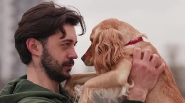 Sakallı bir adam Cocker Spaniel 'i kollarında tutuyor ve gözlerine bakıyor. Yeşil kazaklı bir adam köpeğine bir şey söylüyor ve ona sarılıyor. Yüksek kalite 4k görüntü