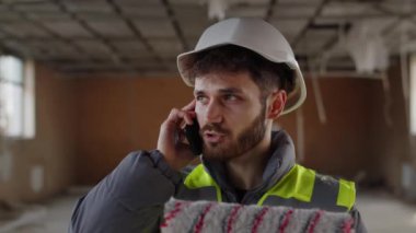 İnşaat alanında beyaz kasklı bir adam telefonda konuşuyordu. Boya silindirli müteahhit telefonla yapılan işi ustabaşına bildiriyor. Yüksek kalite 4k görüntü