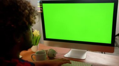 Kıvırcık saçlı bir adam monitörün önünde oturur ve beyaz bardaktan kahve içer. Bir adam ev ofisinde otururken uzaktan bilgisayarın başında çalışıyor. Yüksek kalite 4k görüntü
