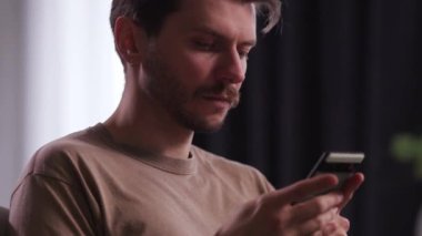 Sakallı genç bir adam akıllı telefon kullanır. Kahverengi tişörtlü bir adam elinde bir telefon tutuyor ve bir mesaj yazıyor. Yüksek kalite 4k görüntü