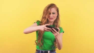 Uzun kızıl saçlı çekici kadın akıllı telefonuyla cep telefonu oyunu oynamaya odaklanmış. Yeşil tişörtlü kızıl saçlı bir kadın, mobil bir oyunda zor bir aşamayı tamamladıktan sonra seviniyor. Yüksek