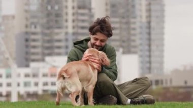 Genç sakallı bir adam kendisine doğru koşan bir cocker spanyel 'i kucaklıyor. Çimlerin üzerinde oturan bir adam bir köpeğe sarılıyor ve ona bir şey söylüyor. Yüksek kalite 4k görüntü