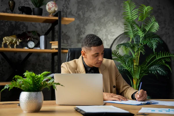 若いアフリカ系アメリカ人実業家が自宅のオフィスに座り 様々な契約書にサインしている 金融会社の取締役は 最後の四半期の報告書を調べます 高品質の写真 — ストック写真