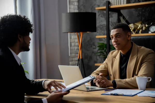 アフリカ系アメリカ人のビジネスマンがテーブルに座り 仕事を報告する従業員の話を聞く 2人の起業家が新しいスタートアップのために資金を調達する方法を議論している — ストック写真