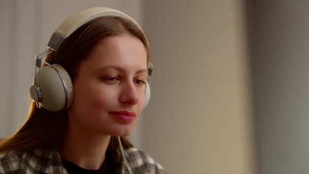 Uśmiechnięta Dziewczyna Siedzi Przed Monitorem Słucha Muzyki Słuchawkach Brunetka Słucha — Wideo stockowe