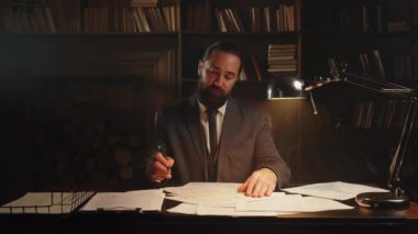 Takım elbiseli bir adam masaya oturur ve belgeleri imzalar. Sakallı bir erkek işadamı ofisinde oturuyor ve çeşitli belgeleri imzalıyor. Yüksek kalite 4k görüntü