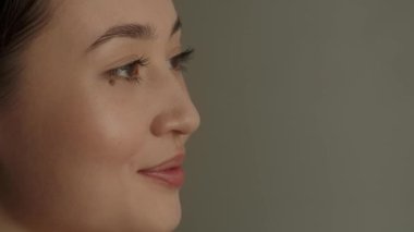 Gözünün altında ben olan genç bir kadın kameraya poz veriyor. Gri arka planda poz veren güzel gülümseyen Asyalı kadın. Yüksek kalite 4k görüntü