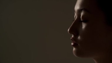 Genç bir kadın loş bir odada gözleri kapalı duruyor. Kahverengi arka planda poz veren güzel bir Asyalı kadın. Yüksek kalite 4k görüntü