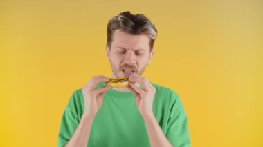Genç adam önce kokluyor, sonra pastayı ısırıyor ve onaylamayan bir şekilde başını sallıyor. Yeşil tişörtlü bir adam pastasının tadını beğenmez. Yüksek kalite 4k görüntü
