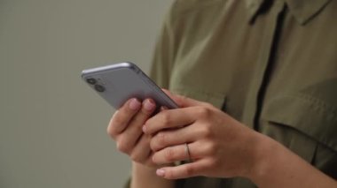 Akıllı telefon kullanan bir kadının görüntüsü kesilmiş. Gri arka planda duran bir kadın akıllı telefonuna mesaj yazıyor. Yüksek kalite 4k görüntü