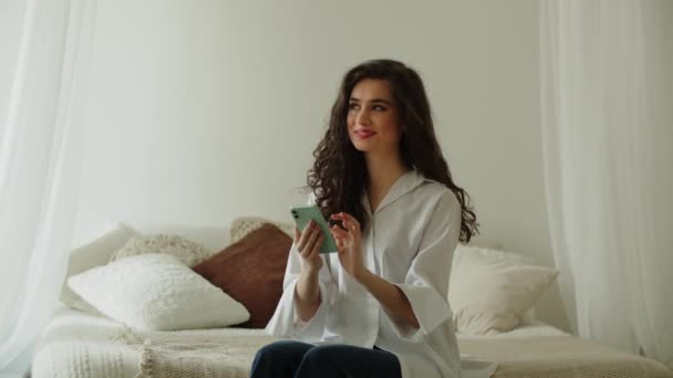 Krásná Dlouhosrstá Bruneta Sedí Posteli Ťuká Obrazovku Chytrého Telefonu Usmívající — Stock video