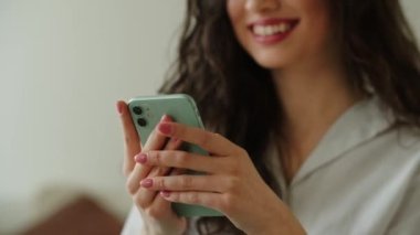 Akıllı telefon ekranını dinleyen gülümseyen kadın görüntüsü. Esmer bir kadın telefonundan haberlere bakıyor. Yüksek kalite 4k görüntü