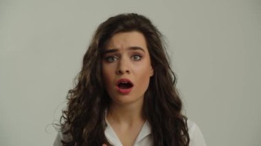 Güzel, uzun saçlı bir esmer gri bir arka planda duruyor ve şaşkınlıkla ağzını açıyor. Genç esmer bir kadın kameraya şaşkınlıkla bakıyor. Yüksek kalite 4k görüntü