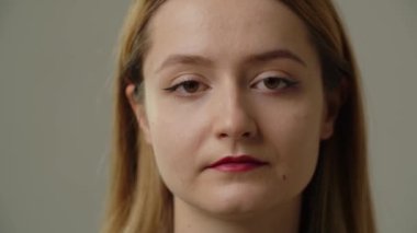 Gri bir duvarın önünde duran uzun saçlı sarışının portresi. Gri arka planda kameraya poz veren güzel bir genç kadın. Yüksek kalite 4k görüntü