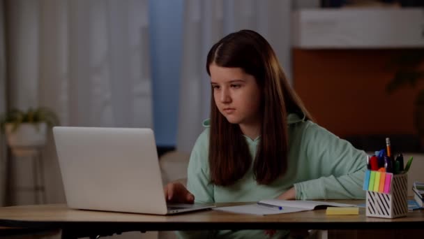 一个黑发女孩坐在桌旁 在她的笔记本电脑上上网 这个女孩在电脑上使用因特网做作业 高质量的4K镜头 — 图库视频影像