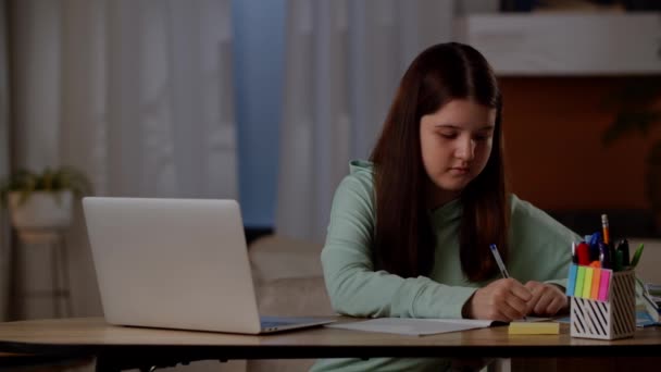 소녀는 노트북 탁자에 앉아서 노트북에 무엇인가를쓰고 있습니다 소녀는 컴퓨터를 사용하여 — 비디오