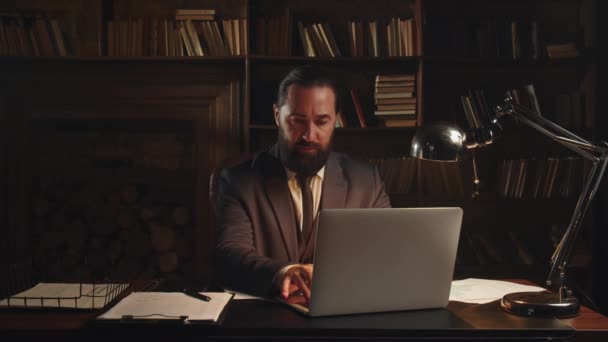 一位男性创业者坐在家里的办公室里 在笔记本电脑前远程工作 一个穿着西装的大胡子男人坐在桌旁 在笔记本电脑上打字 高质量的4K镜头 — 图库视频影像