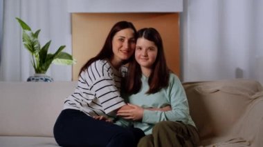 Anne ve kızı kanepede oturur ve gülümseyerek kameraya bakarlar. Esmer bir kadın kızına sarılıyor ve onu yanağından öpüyor. Yüksek kalite 4k görüntü