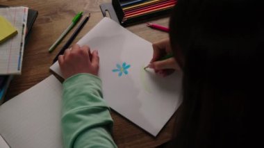 Bir kız masaya oturur ve bir yaprak kağıda çiçek çizer. Kız boş zamanını renkli kalemlerle çizerek geçiriyor. Yüksek kalite 4k görüntü