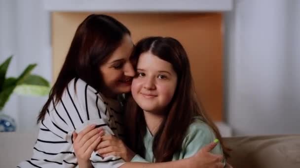 一个穿着条纹毛衣的微笑的女人坐在沙发上拥抱她的女儿 一位慈爱的母亲拥抱她的女儿 亲吻她的脸颊 高质量的4K镜头 — 图库视频影像