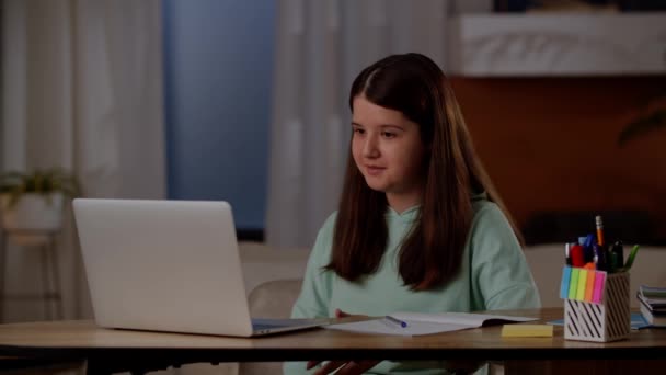 一个小女孩坐在房间里 通过笔记本电脑摄像头与一位导师交流 一个黑发女孩坐在笔记本电脑前的桌子旁 在在线课上与一位老师交流 — 图库视频影像
