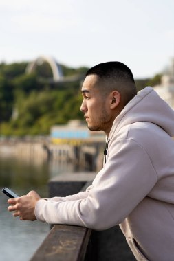 Asyalı bir adam setin üzerinde duruyor, korkuluklara yaslanıyor ve uzaklığa bakıyor. Genç bir adam elinde telefonla setin kenarında duruyor ve nehrin manzarasına hayran. Yüksek