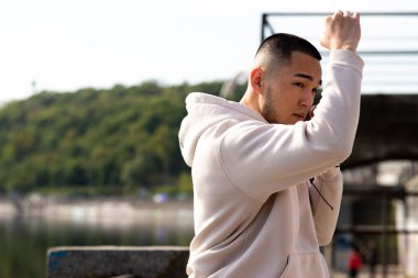 Eşofmanlı genç bir adam dışarıda duruyor ve yumruklarını önünde tutuyor. Asyalı bir adam dövüşmek için kameranın önünde duruyor. Yüksek kalite fotoğraf