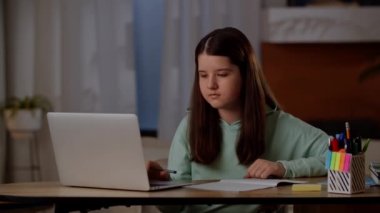 Küçük bir kız ödevini bilgisayarda yapıyor. Çocuk evde bir dizüstü bilgisayarla çevrimiçi öğrenme ile meşgul. Yüksek kalite 4k görüntü
