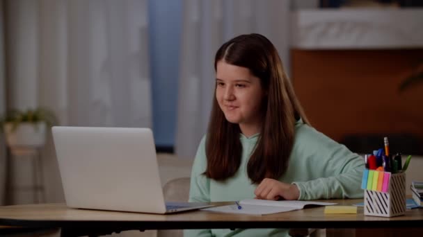 这个女孩正坐在桌旁 向笔记本电脑的摄像头挥手 一个女孩在网上课上和一个家庭教师谈话 高质量的4K镜头 — 图库视频影像