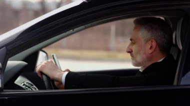 Takım elbiseli gri saçlı bir adam bir arabanın direksiyonunda oturur ve akıllı telefon ekranını dinler. Sakallı bir iş adamı akıllı telefon kullanır ve trafik sıkışıklığının geçmesini bekler. Yüksek