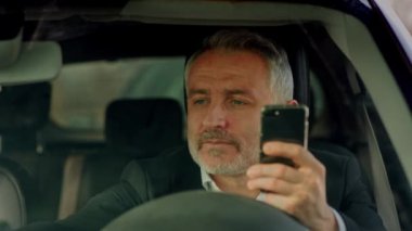 Gri saçlı, sakallı bir adam arabada oturur ve kahve içer. Takım elbiseli bir adam arabada oturmuş akıllı telefondan haberleri okuyor ve fincandan kahve içiyor. Yüksek kalite 4k görüntü